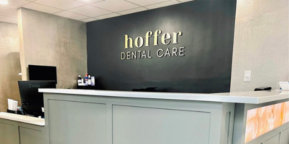 The image shows an interior view of a dental care office named Hoffer Dental Care. The space appears modern and clean, with a reception area featuring a counter, signage, and a waiting room.