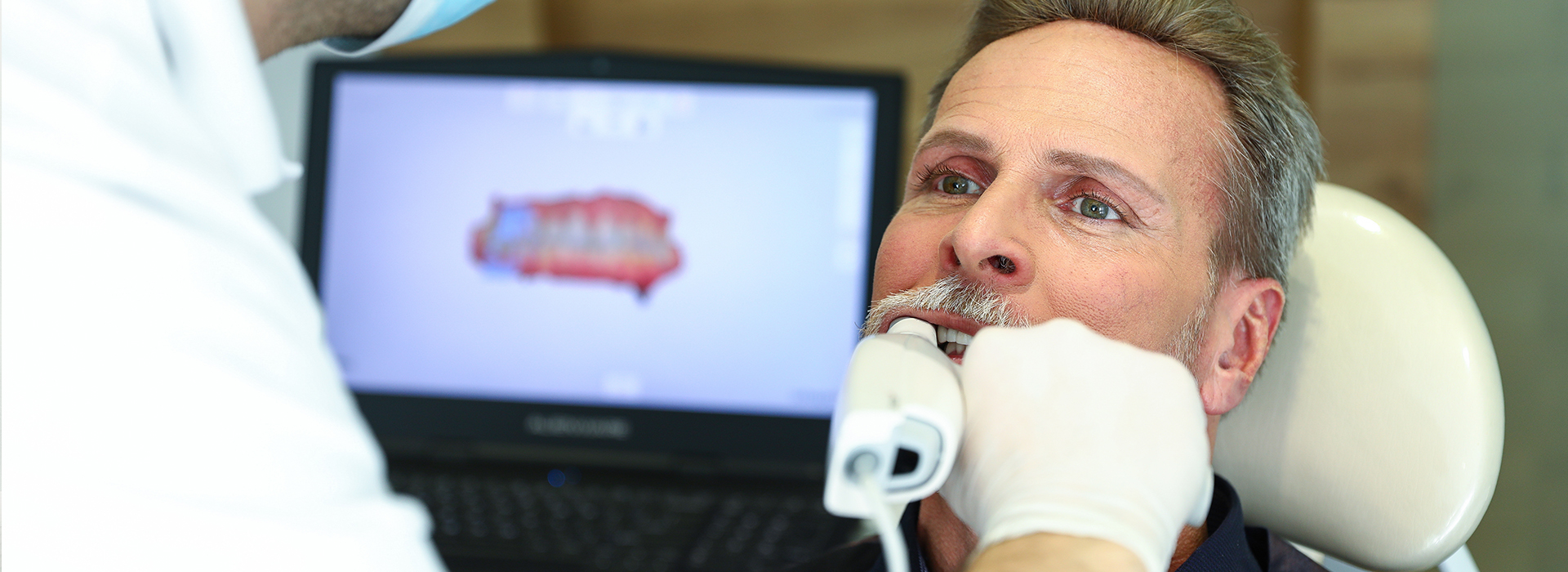A man receiving a dental treatment, with a dental professional using a computer screen to guide the procedure.