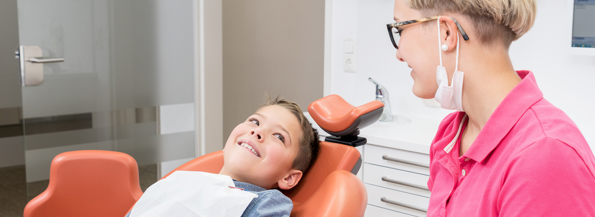 A person sitting in a dental chair, smiling at the camera, with a dental professional standing beside them.