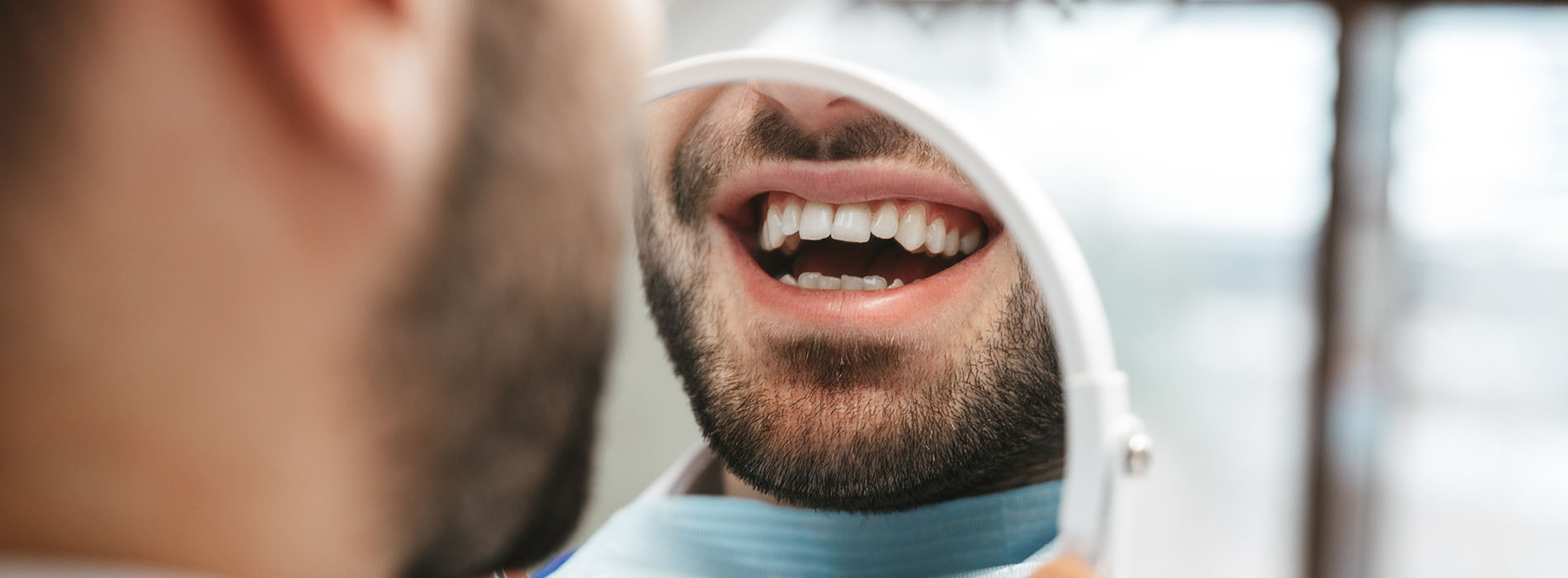 The image shows a person with a toothy smile, seemingly in the process of having their teeth cleaned or checked by another individual who is not fully visible.