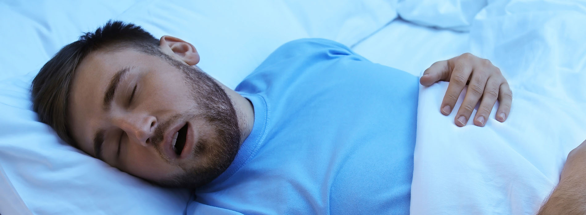 The image depicts a man lying in bed with his eyes closed, suggesting he is sleeping or possibly asleep.